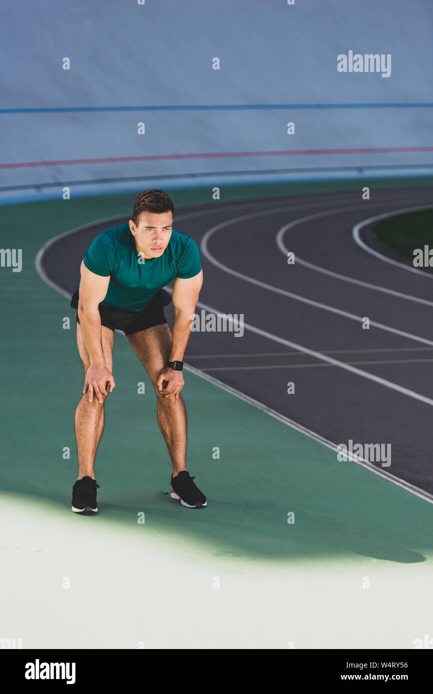 mixed race sportsman with hands on knees standing at stadium Stock Photo
