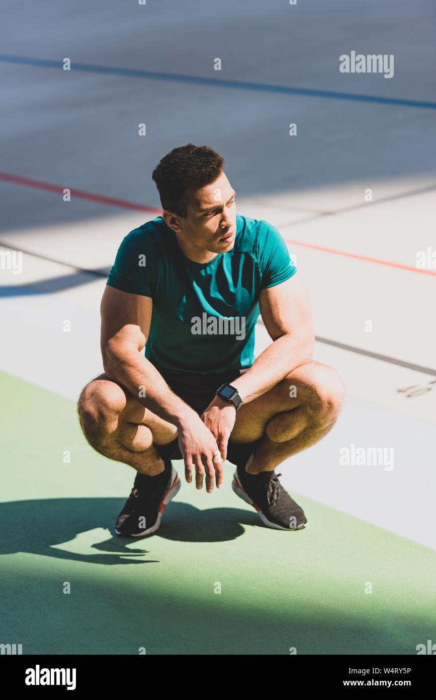 muscular mixed race sportsman squatting at stadium in sunlight Stock ...