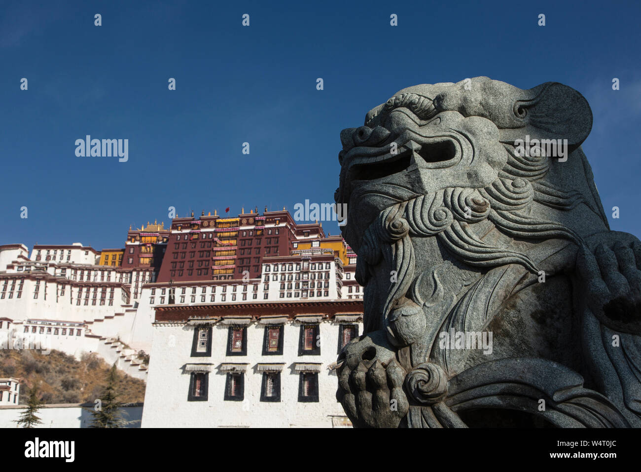 China, Tibet, Lhasa, A carved stone lion statue in front of the Potala Palace  founded about 1645 AD and was the former summer palace of the Dalai Lama and is a part of the Historic Ensemble a UNESCO World Heritage Site. Stock Photo