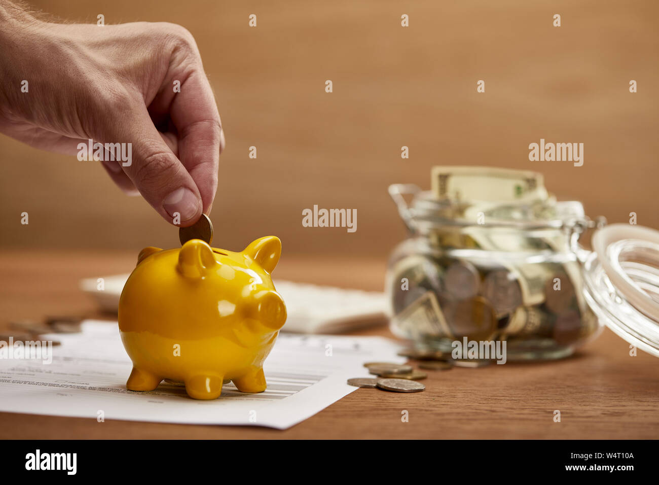 cropped view of man putting coin in yellow piggy bank Stock Photo - Alamy