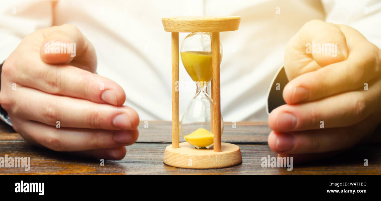 Man protects the hourglass. Concept of saving time and money. Time management. Planning work. Reduced cost and bureaucratic burden. Saving productivit Stock Photo