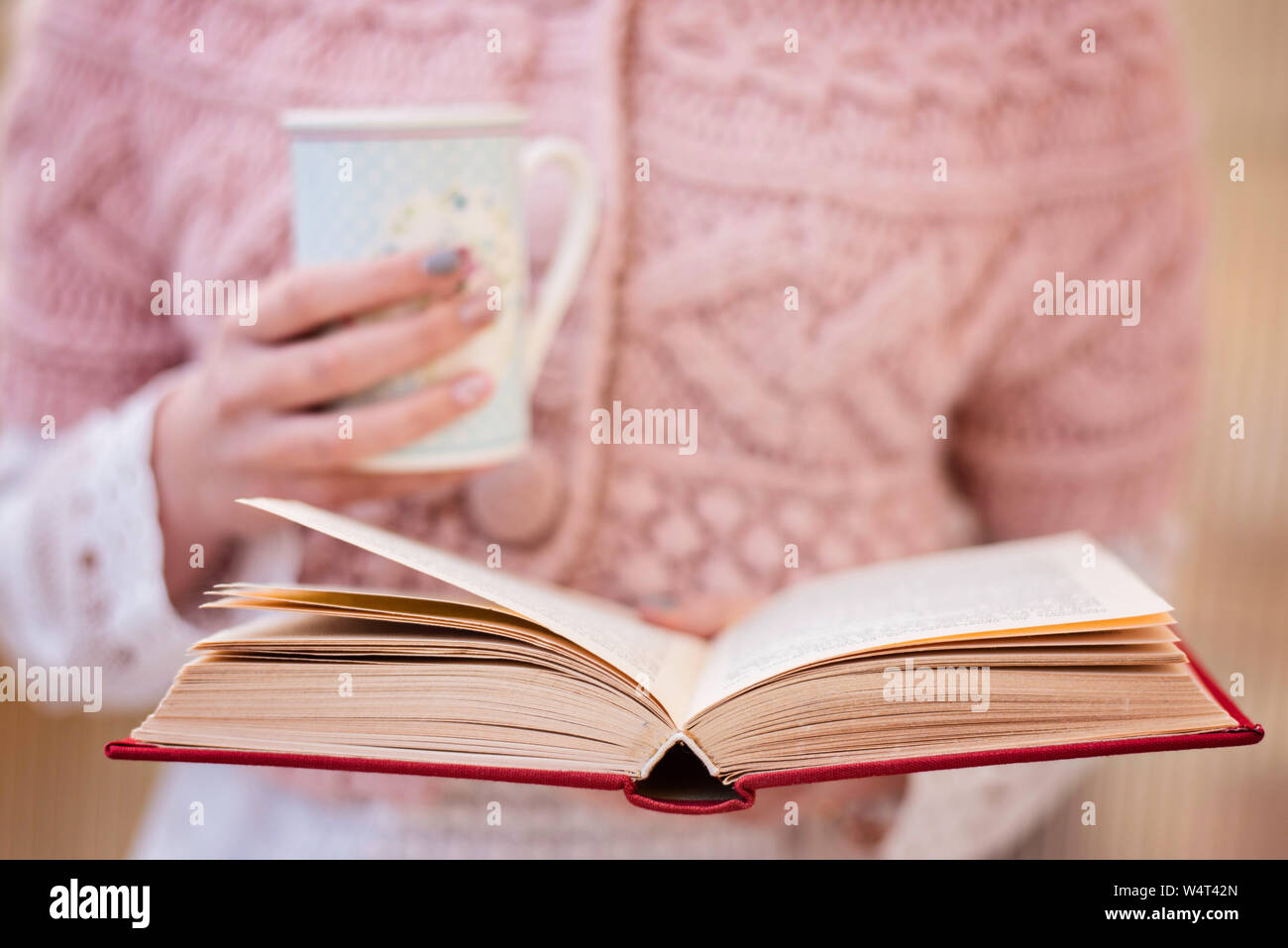 Teenage girl reading a book and drinking a cup of tea Stock Photo