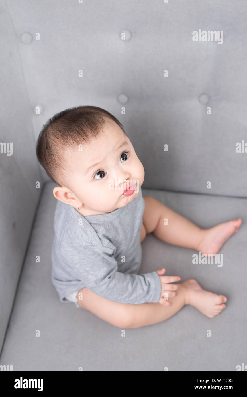 childhood, babyhood and people concept - happy little baby girl sitting on sofa at home Stock Photo