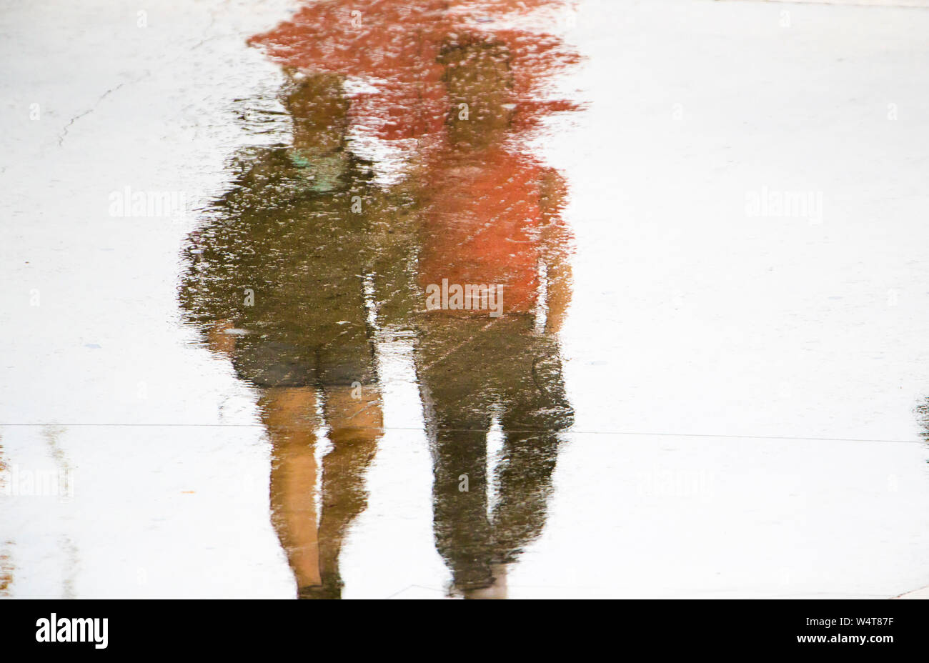 Blurry reflection silhouette in a puddle of couple holding hands while walking on a rainy summer day Stock Photo