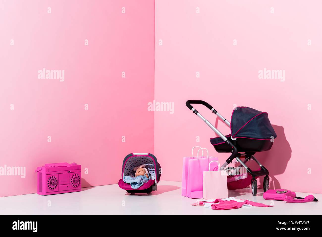 baby carriage, doll in baby carrier, shopping bags and boombox on pink Stock Photo