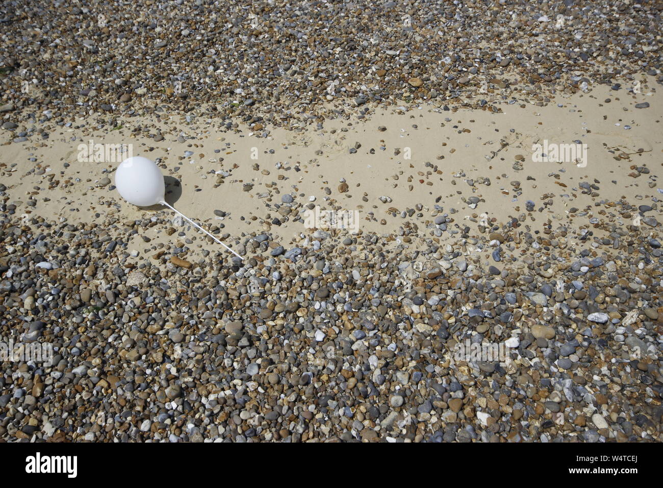 solitary white balloon lying on a pebble and sand beach Stock Photo