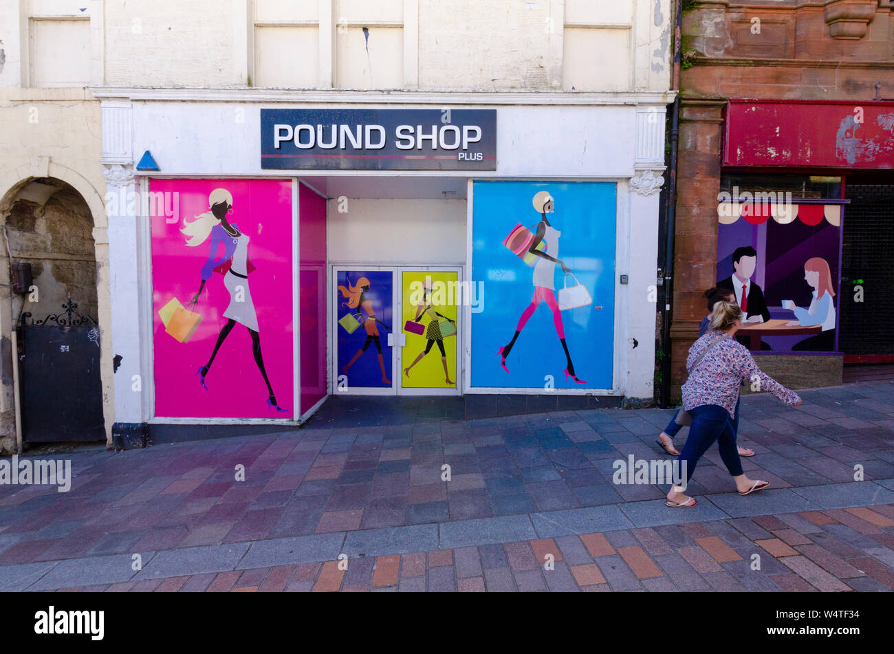 People pass by empty retail units in the High Street in Dumfries Scotland UK. Artwork has been painted on them as they have not been let for some time Stock Photo