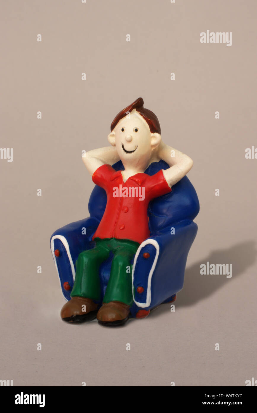 Plastic model caricature of a young man relaxing in an armchair against a plain background. Stock Photo