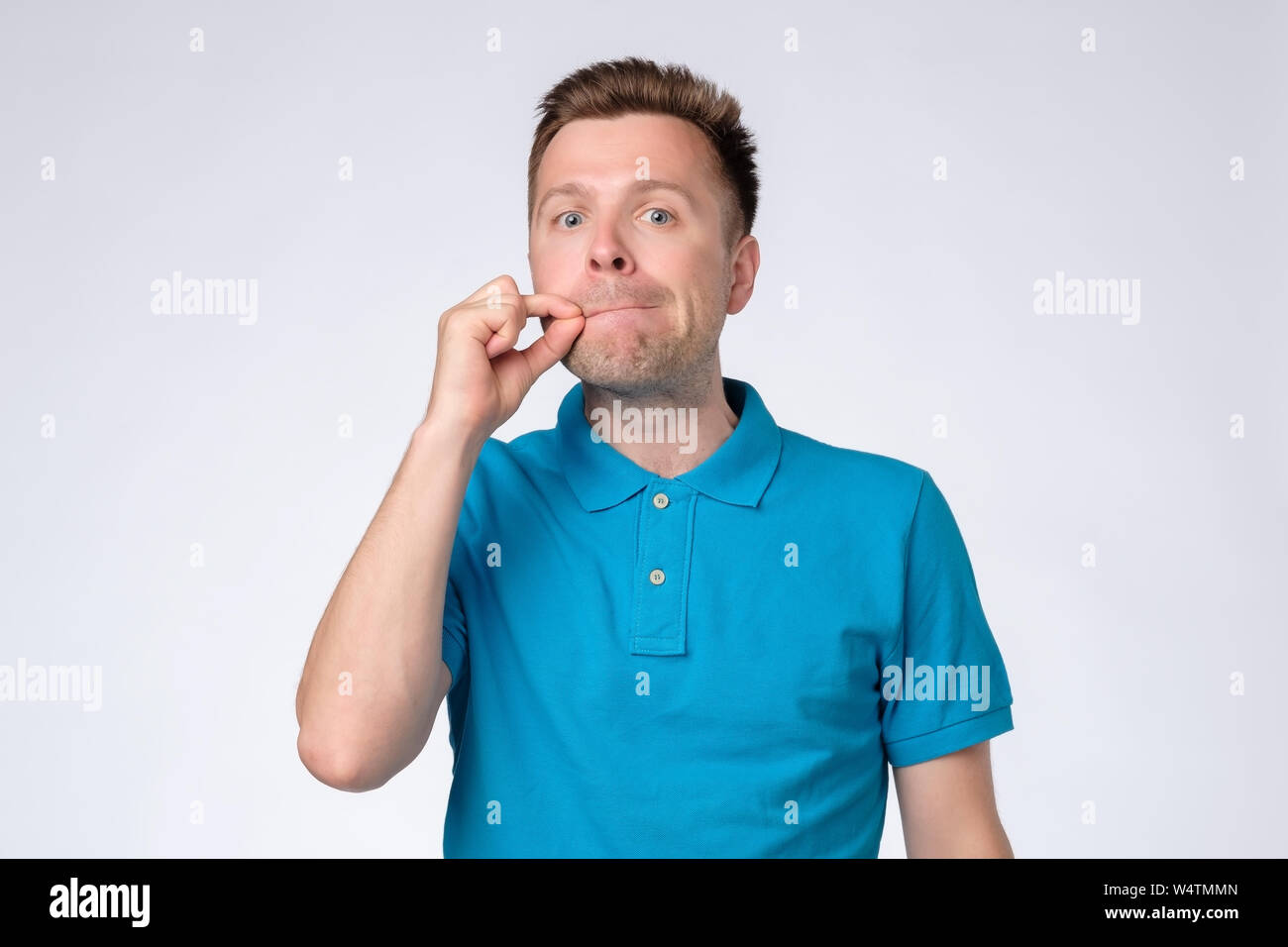 Young man closing mouth and lips shut as zip with fingers. Stock Photo