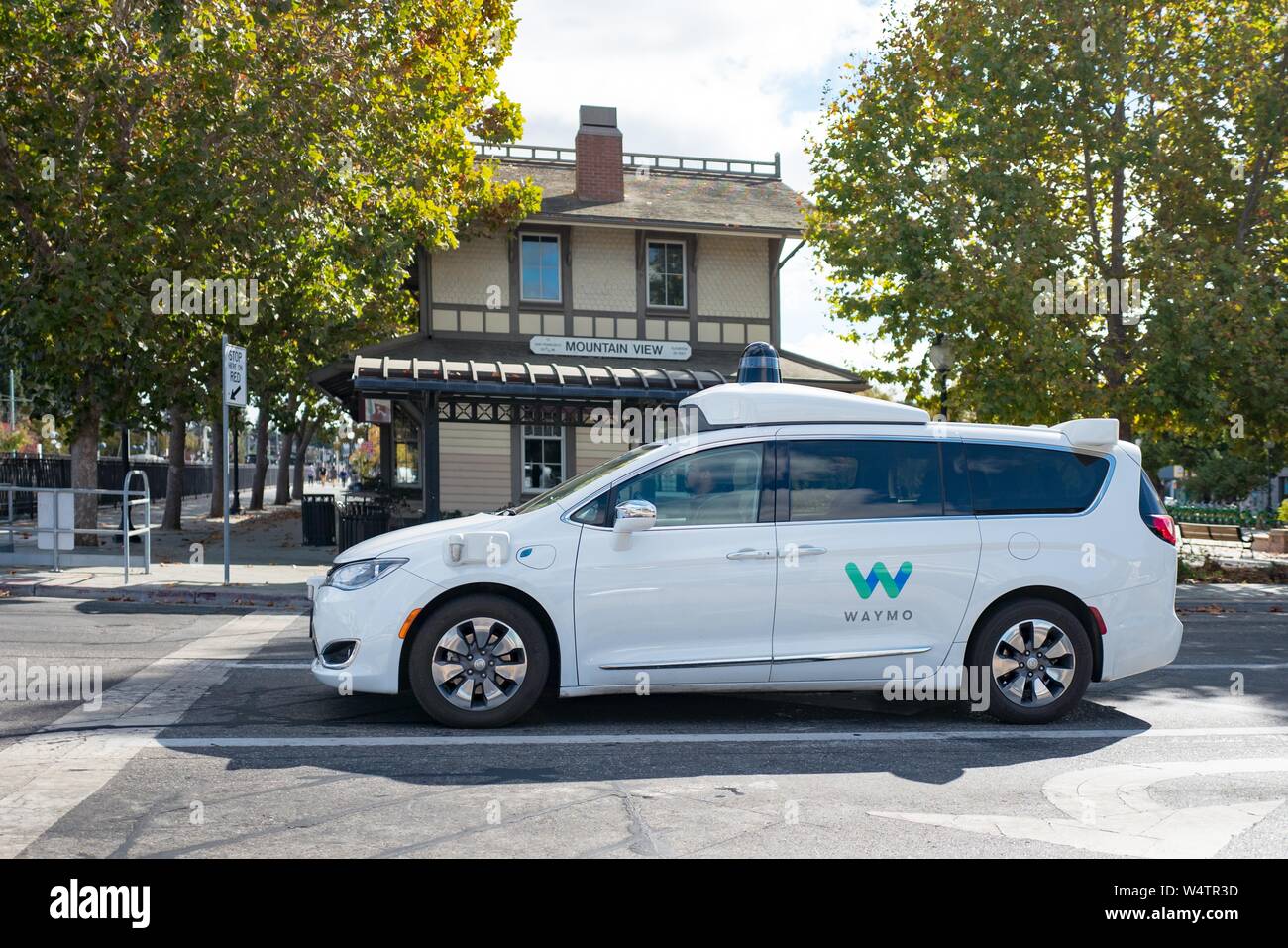 Close-up of self driving minivan, with LIDAR and other sensor units and logo visible, part of Google parent company Alphabet Inc, driving past historic railroad station with sign reading Mountain View, in the Silicon Valley town of Mountain View, California, with safety driver visible, October 28, 2018. () Stock Photo