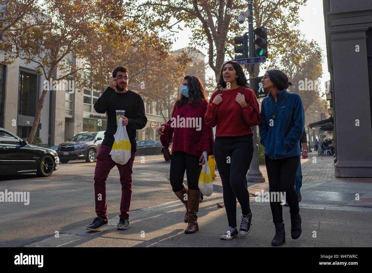 A group of Millennial generation friends holds takeout food bags and walks down University Avenue in the Silicon Valley, Palo Alto, California, with one woman wearing a surgical mask to protect against wildfire smoke from the 2018 Camp Wildfire, November 17, 2018. () Stock Photo
