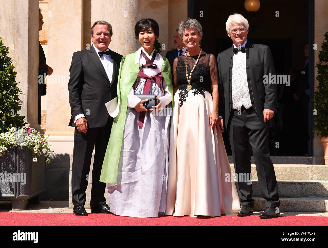 Bayreuth, Germany. 25th July, 2019. The Lord Mayor of Bayreuth Brigitte Merk-Erbe (2nd from right) and her husband Thomas (r) welcome former Chancellor Gerhard Schröder (SPD) and his wife Soyeon Kim to the beginning of the Bayreuth Festival 2019. The Richard Wagner Festival begins in Bayreuth on Thursday. Numerous celebrities are expected on the red carpet. (To dpa 'Bayreuth Festival start in heat with new 'Tannhäuser'') Credit: Tobias Hase/dpa/Alamy Live News Stock Photo