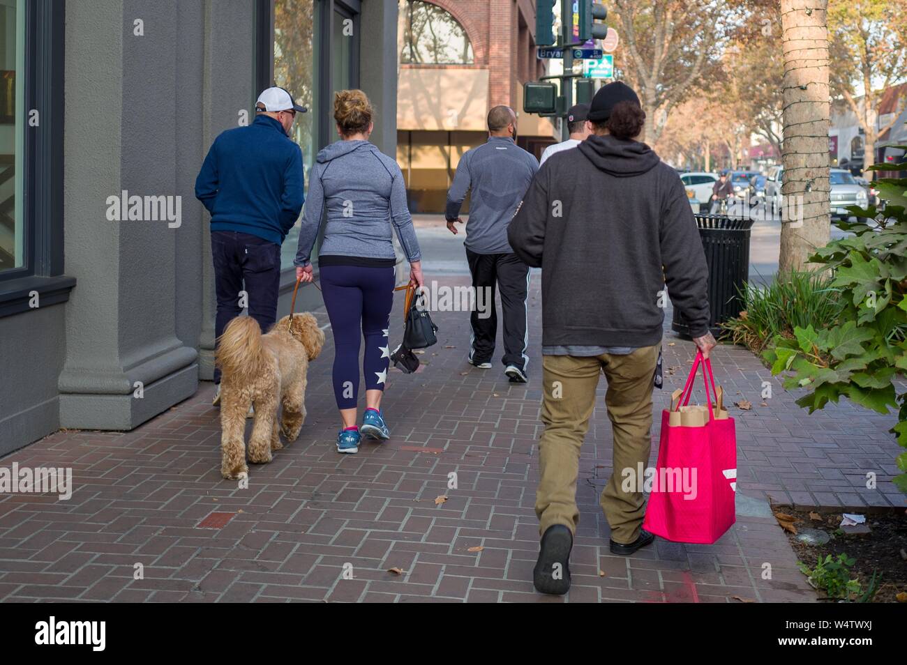 A gig economy worker walks down University Avenue in the Silicon Valley town of Palo Alto, California, carrying the distinctive red bag of food delivery app service Doordash, with bag containing customer order visible, November 17, 2018. () Stock Photo
