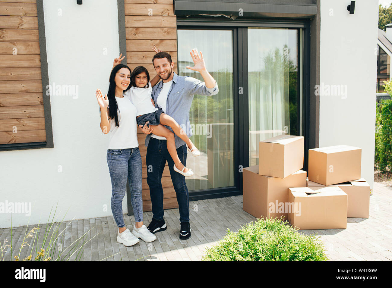 Pretty parent with child bought new home, standing with boxes on backyard house. Moving new house Stock Photo