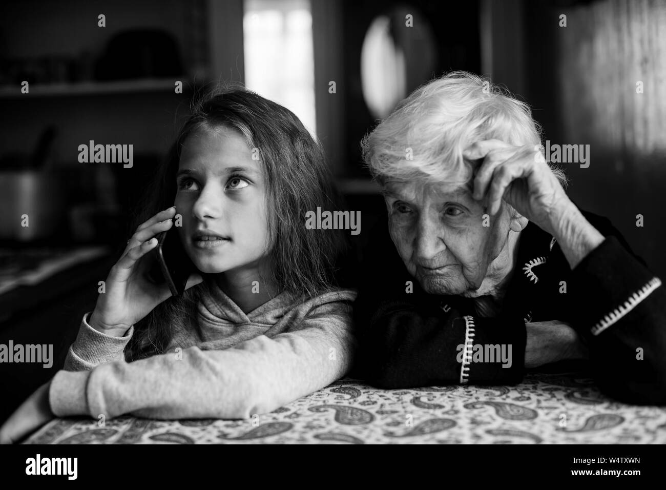 Little girl granddaughter talking on a mobile phone and grandmother her listens. Black and white photo. Stock Photo