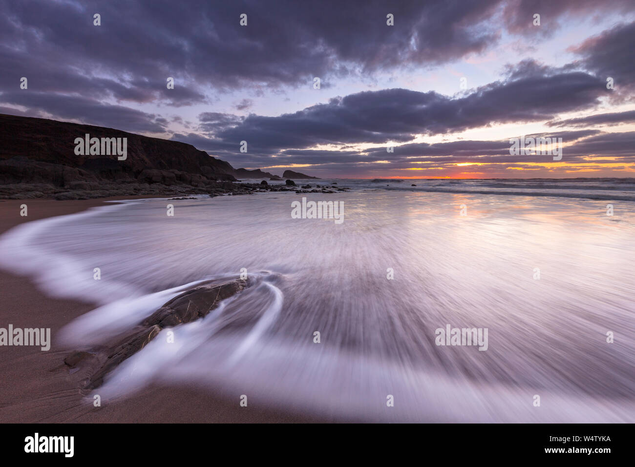 Waves flow over the sand and rocks at Sunset at Welcombe Mouth Beach in North Devon, UK. Stock Photo