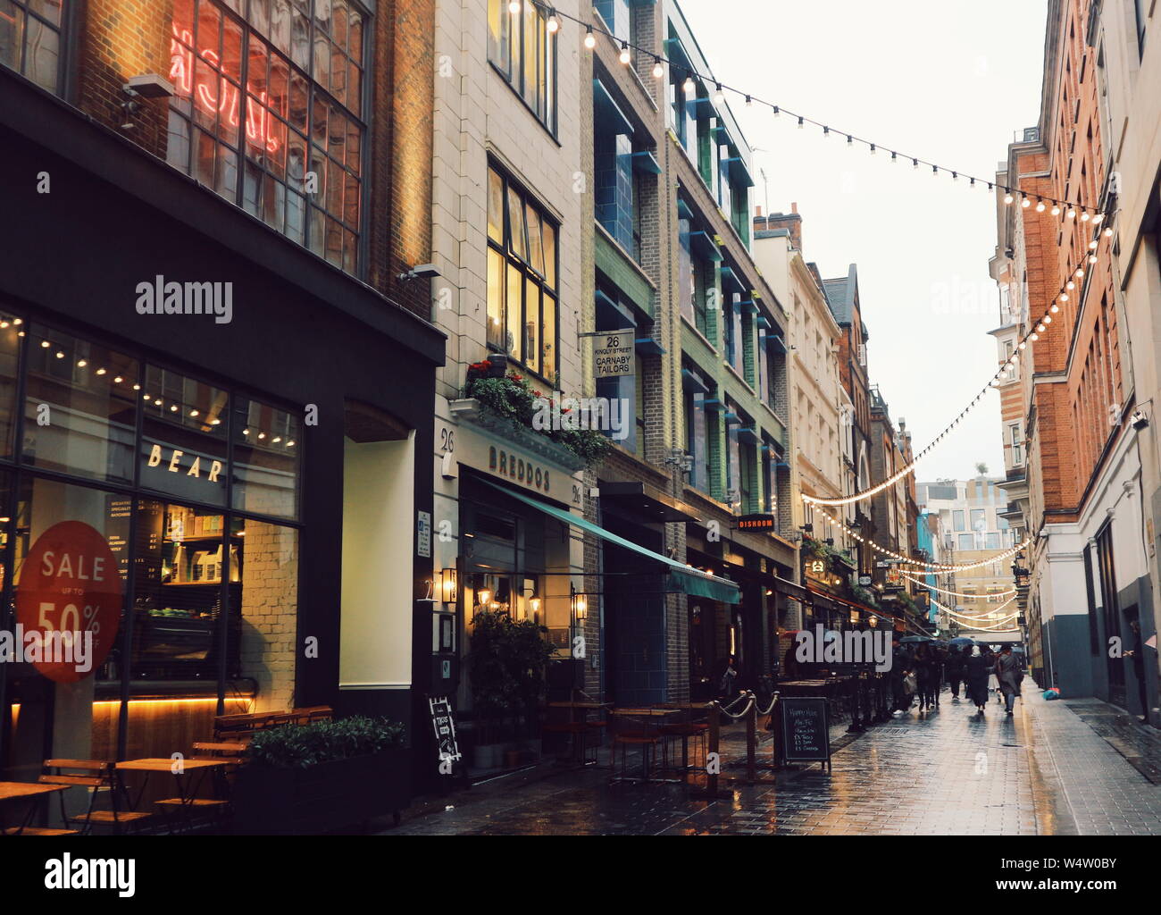 People shopping under the string lights on a rainy day on Kingly Street in Soho, London, UK. Stock Photo