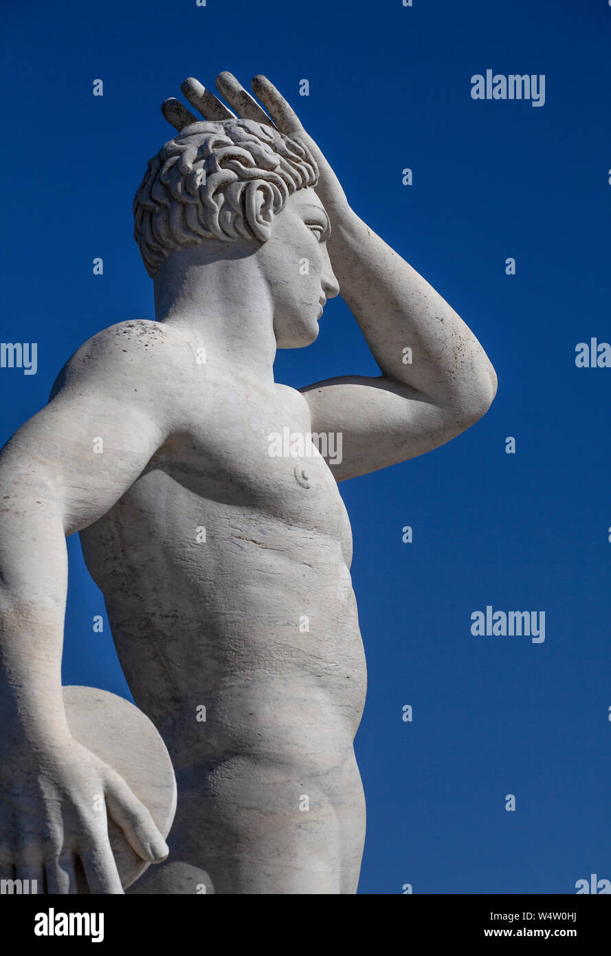 Statue of a discus thrower in the Stadio dei Marmi (Marble Stadium) in Rome. The statue has its hand raised, looking into the distance with a blue sky Stock Photo
