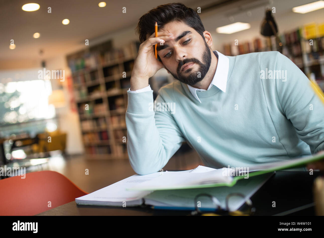Exhausted young man student studying in a library Stock Photo