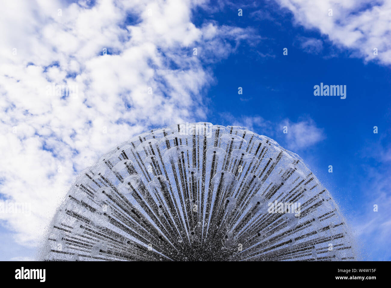 Beautiful circle fountain against blue cloudy sky. A lot of water streams. Abstract photo with copy space. Amazing background. Spraying water around. Stock Photo