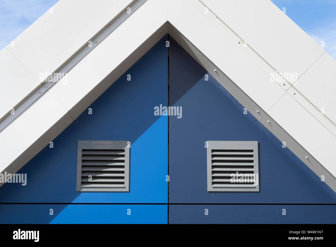 Light and dark blue panels with ventilation grilles on the gable end of a new modern building