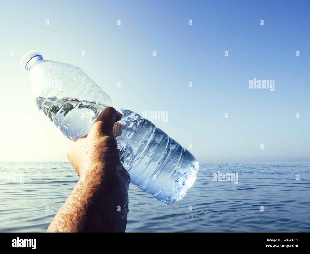 plastic waste at the ocean, hand holding a plastic bottle in the