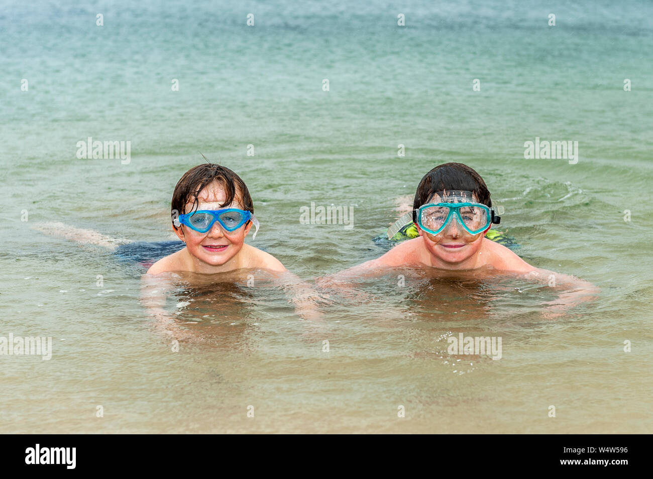 Bantry, West Cork, Ireland. 25th July, 2019. Despite there being no heatwave in Ireland, these local boys, Donnacha and Lucas Cronin-Murphy from Bantry, weren't put off from playing at the beach in the wind and rain. The rain will continue into the evening with top temperatures of 20 to 25°C. Credit: Andy Gibson/Alamy Live News. Stock Photo