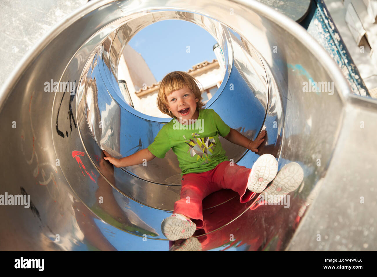 little blond girl playing on a slide on kids playground Stock Photo