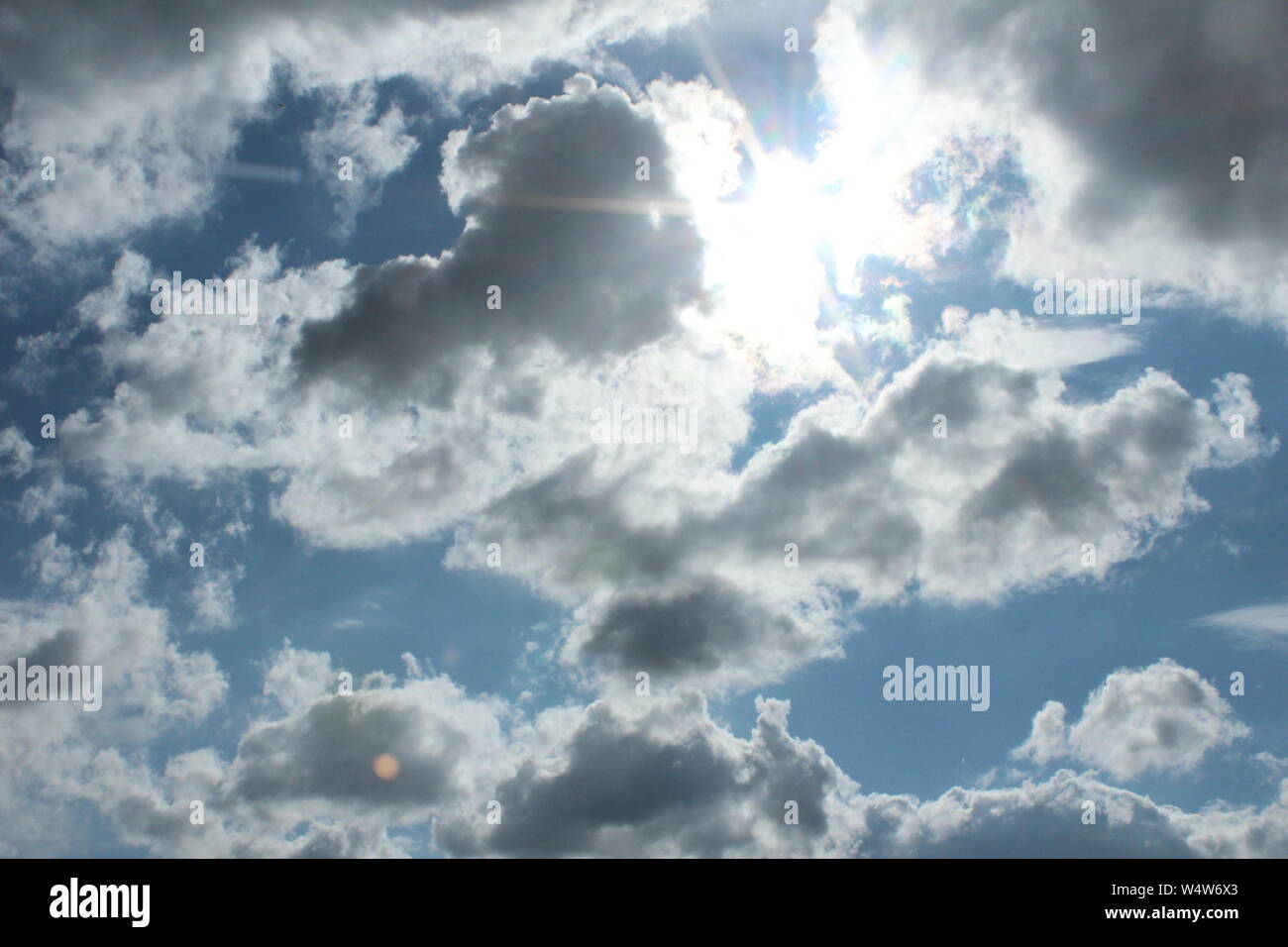 Bright blue sky, with sun coming through white clouds Stock Photo