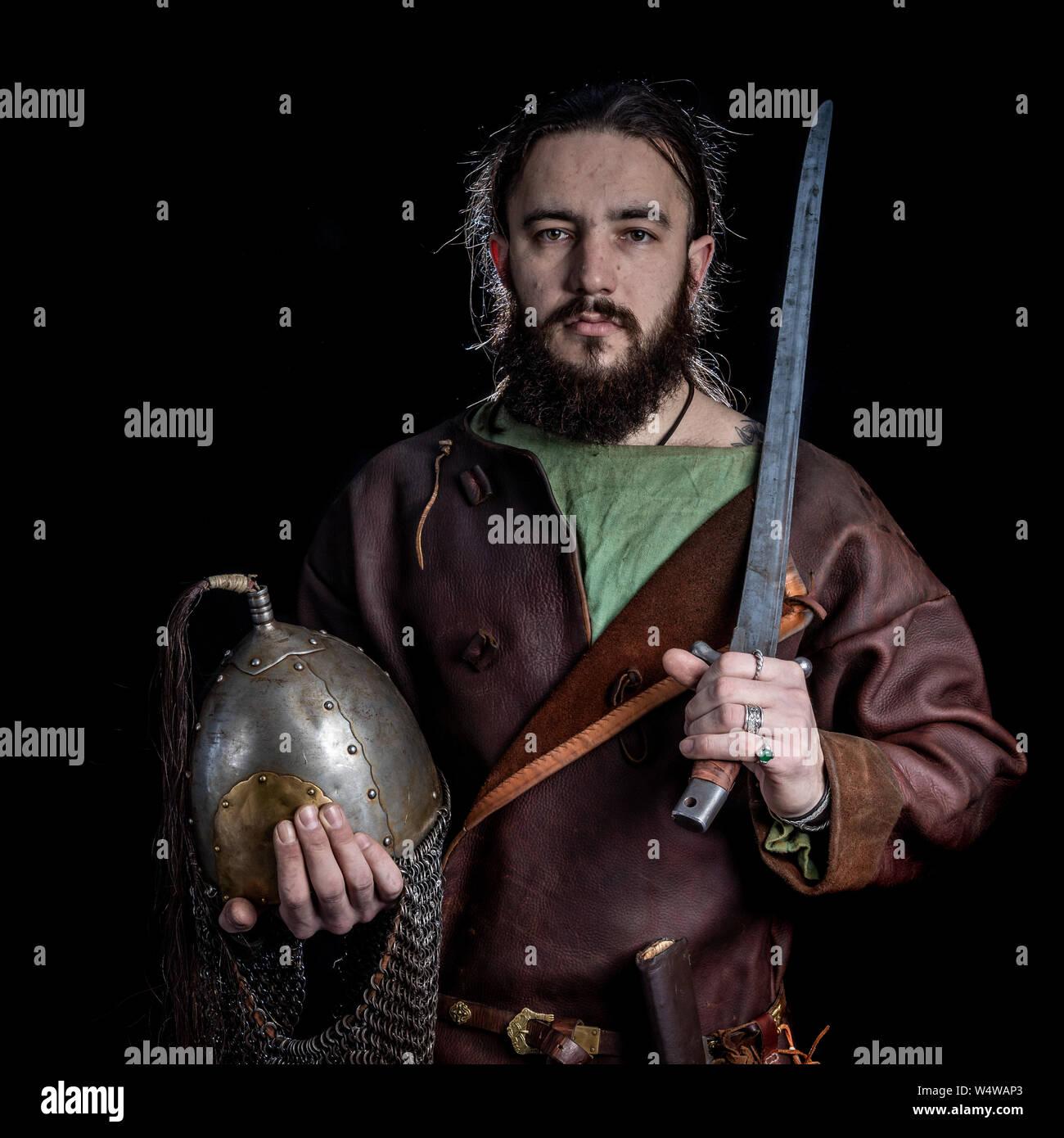 Slavic bearded warrior dressed in leather armor of the Viking Age holding a sword and helmet