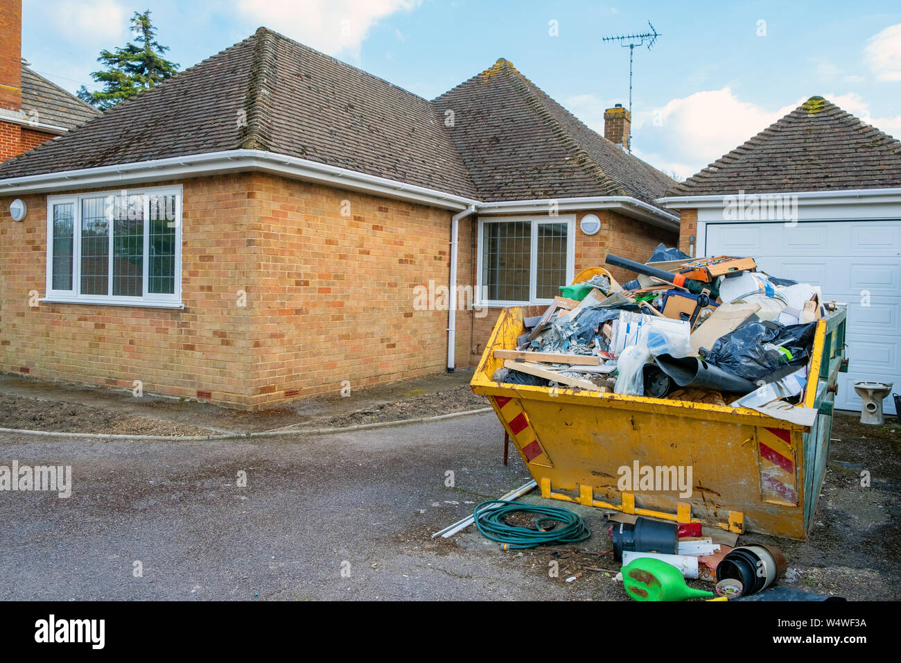 A full yellow rubbish skip on a house driveway. Stock Photo