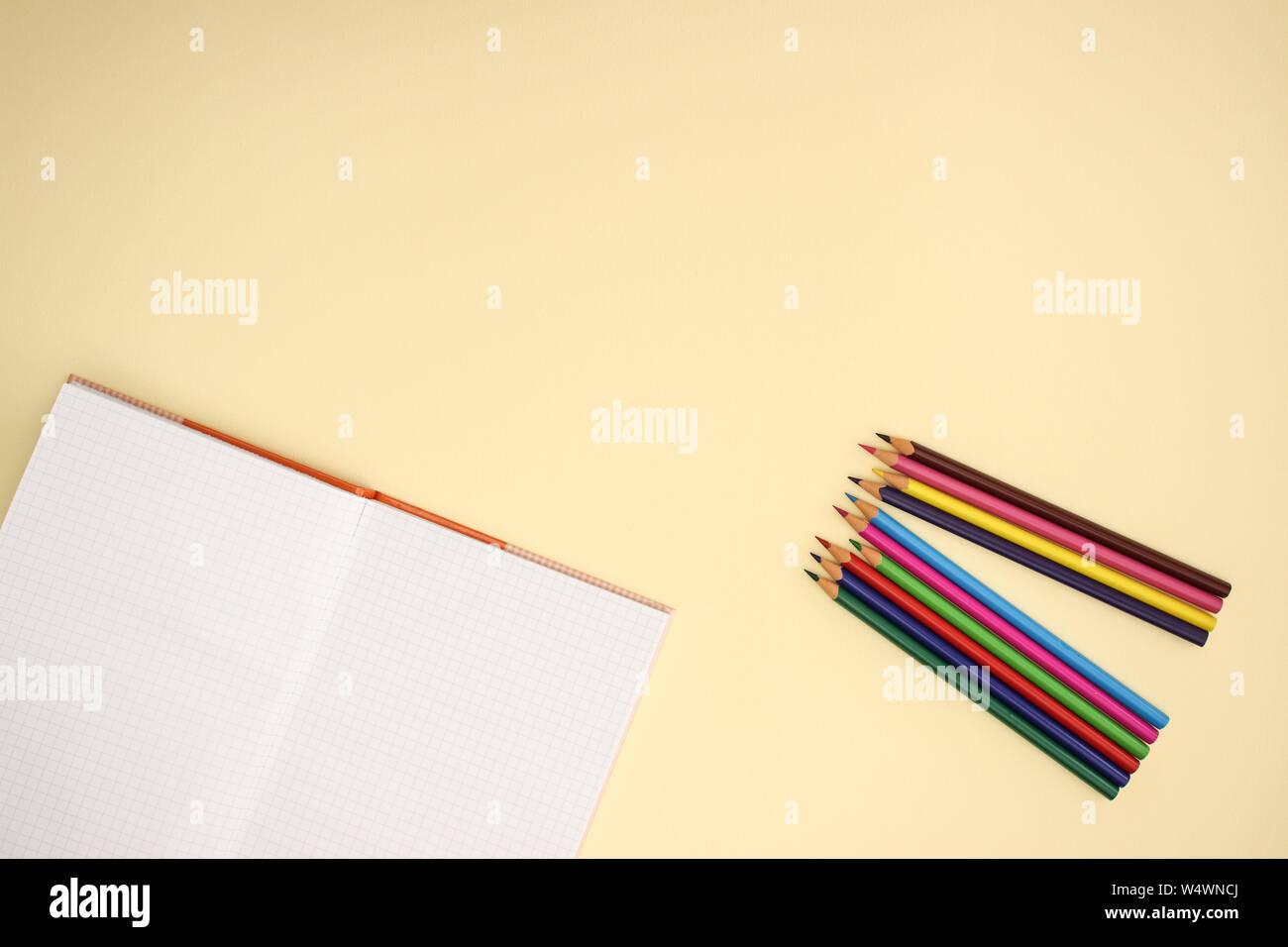 Open notebook and color pencils on yellow background Stock Photo