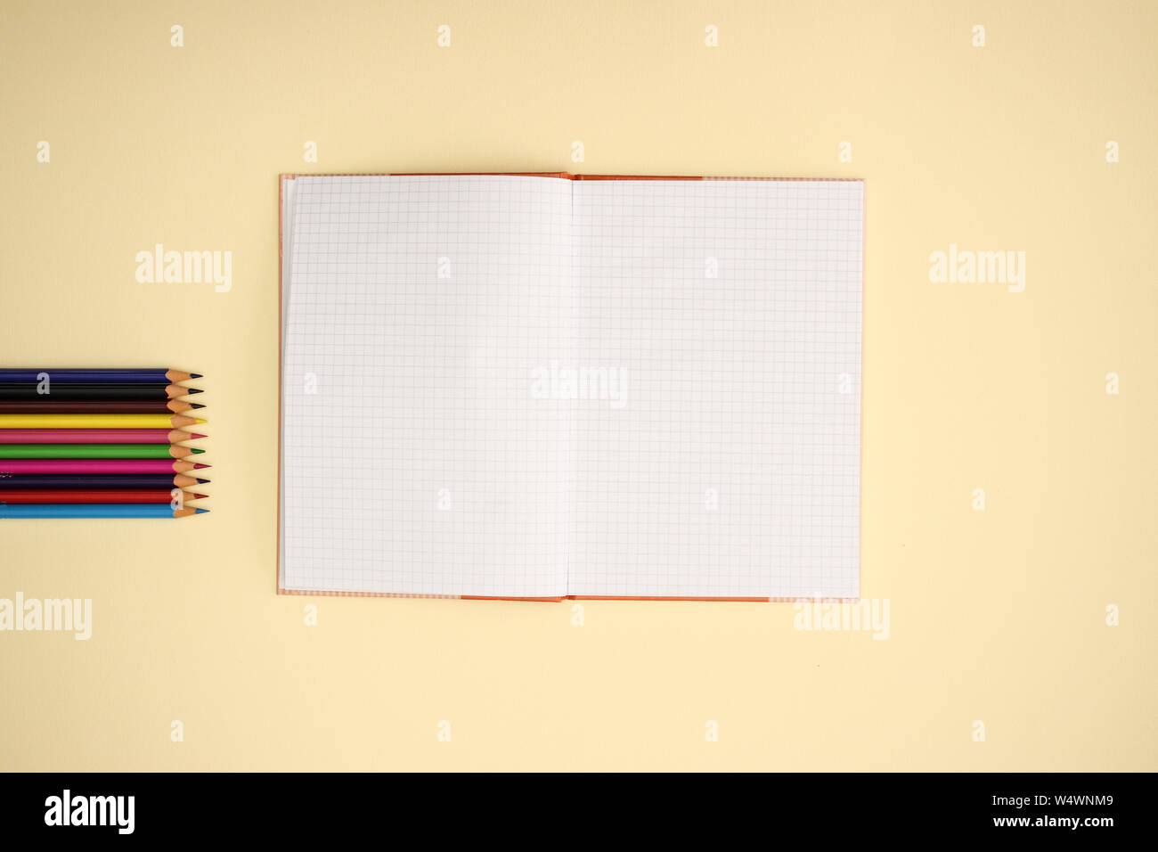 Open notebook and color pencils on yellow background Stock Photo