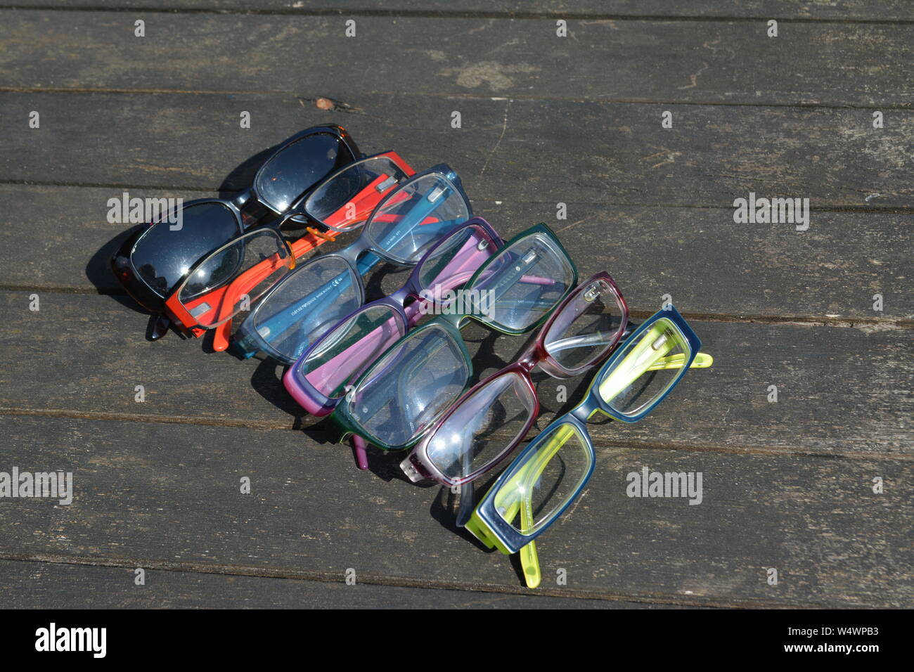 Large number of different framed folded spectacles glasses arranged in a regular pattern on a wooden slatted surface in bright sunlight Stock Photo