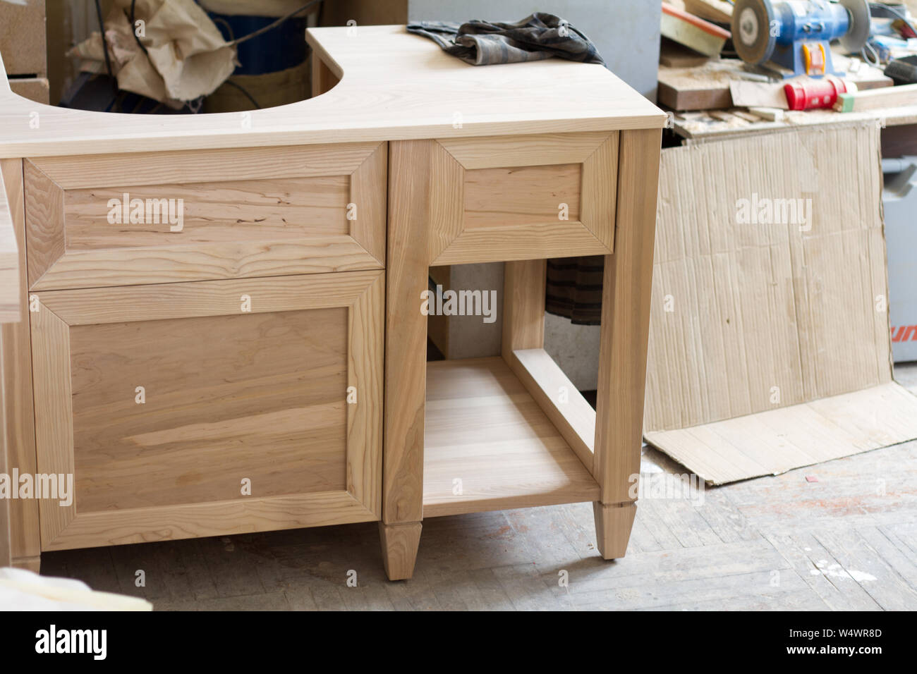 An unfinished wooden kitchen cabinet under the sink on a blurred
