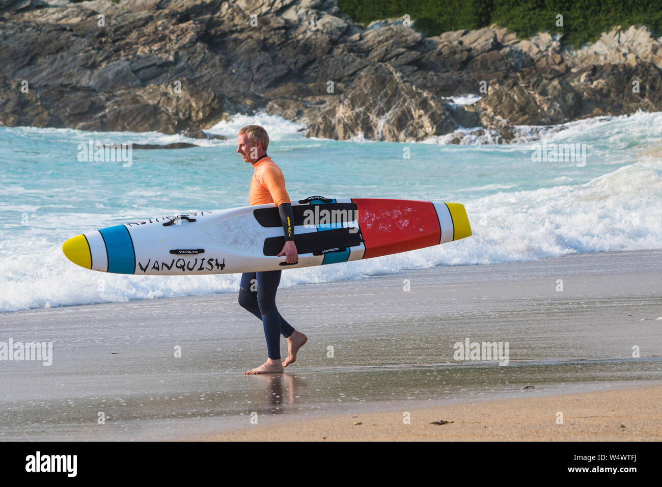A member of Newquay Surf Life Saving Club carrying a Vanquish Life Saving Race Board starting a training session at Fistral in Newquay in Cornwall. Stock Photo