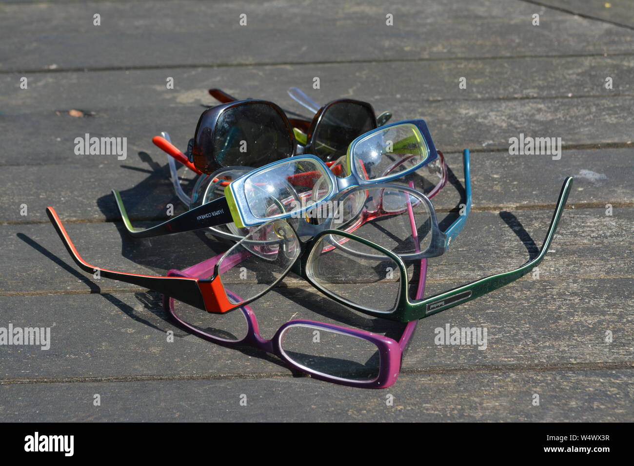 Large number of different framed unfolded spectacles glasses arranged in a random abstract pattern on a wooden slatted surface in bright sunlight Stock Photo