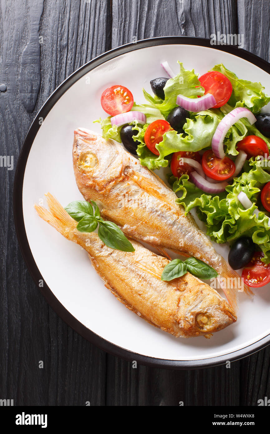 Tasty fried pink dorado or gilt-head bream fish with vegetable salad close-up on a plate on the table. Vertical top view from above Stock Photo