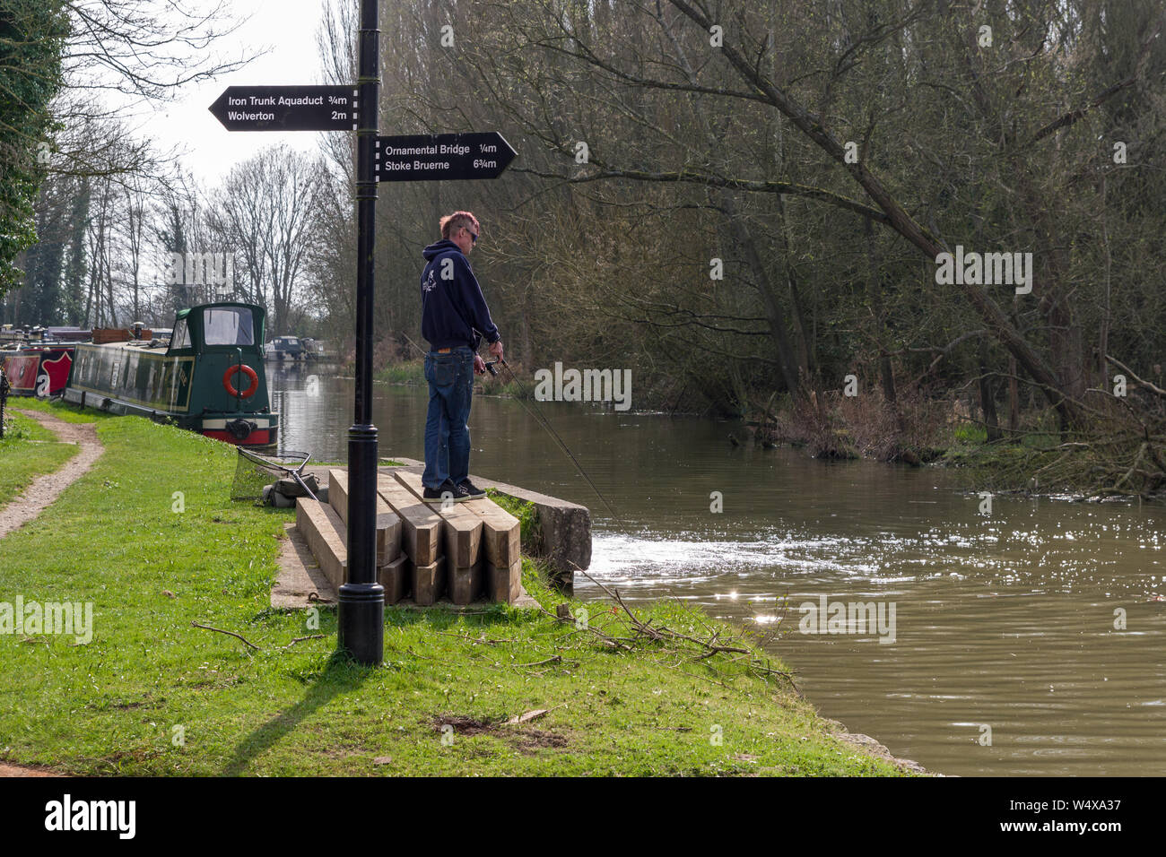 Man standing up and fishing at the junction of the Grand Union canal and Buckingham Arm, Cosgrove, UK Stock Photo