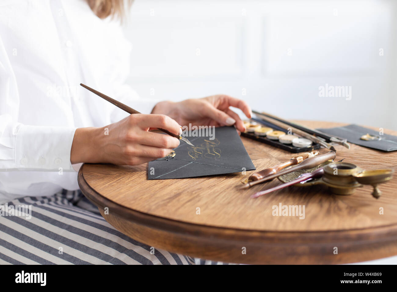 Woman calligrapher is holding a pen with ink and signs a card in ...