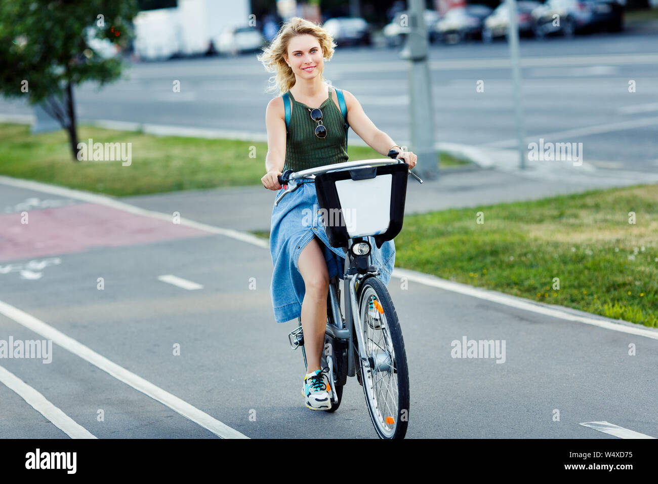 Photo of young blonde in long denim skirt riding bike on road in city