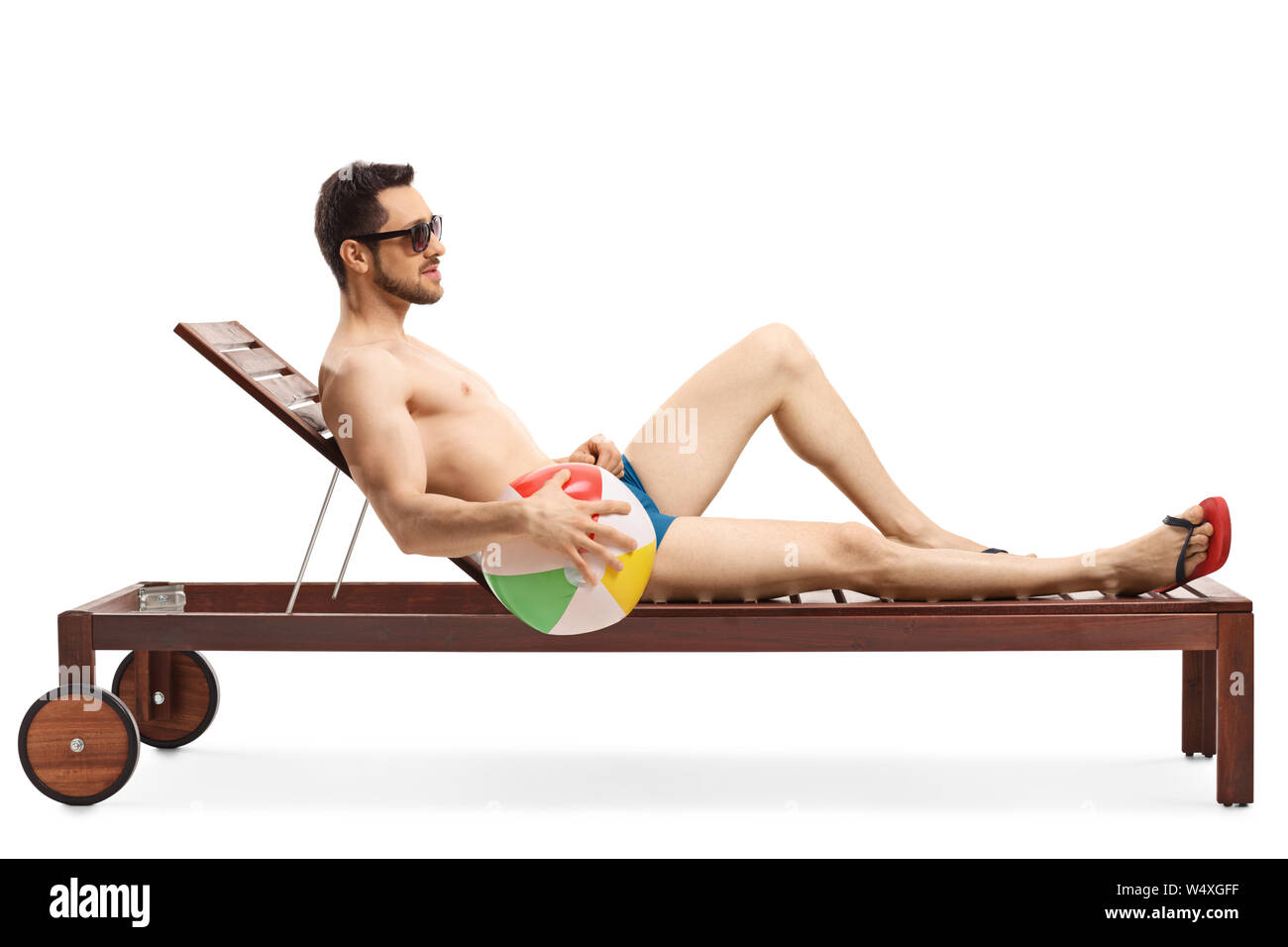 Full length shot of a young fit man on a sunbed holding an inflatable ball isolated on white background Stock Photo