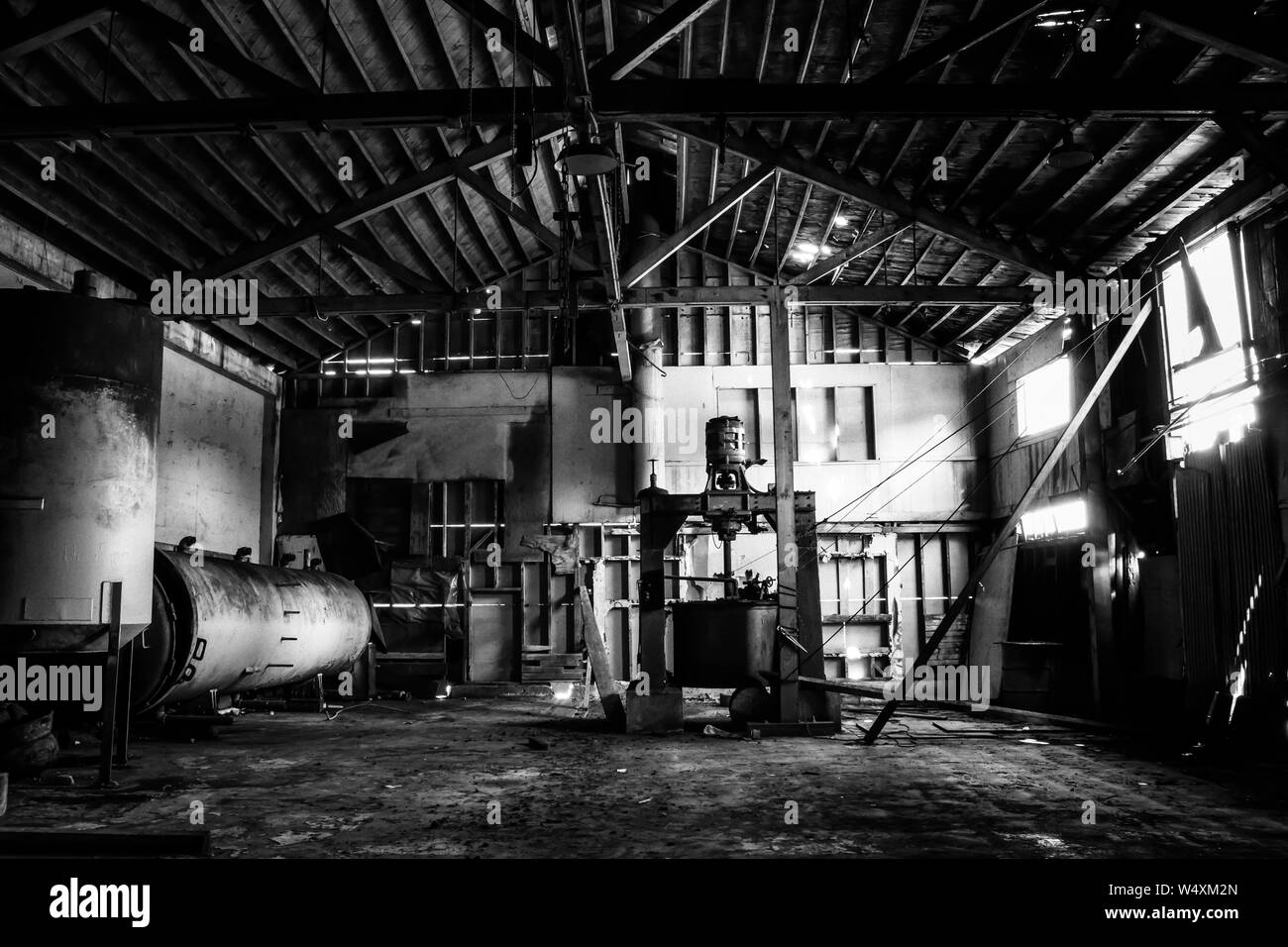 Black and white dramatic interior abandoned cannery warehouse building.  Old equipment and crumbling walls in rustic grungy historic building. Stock Photo