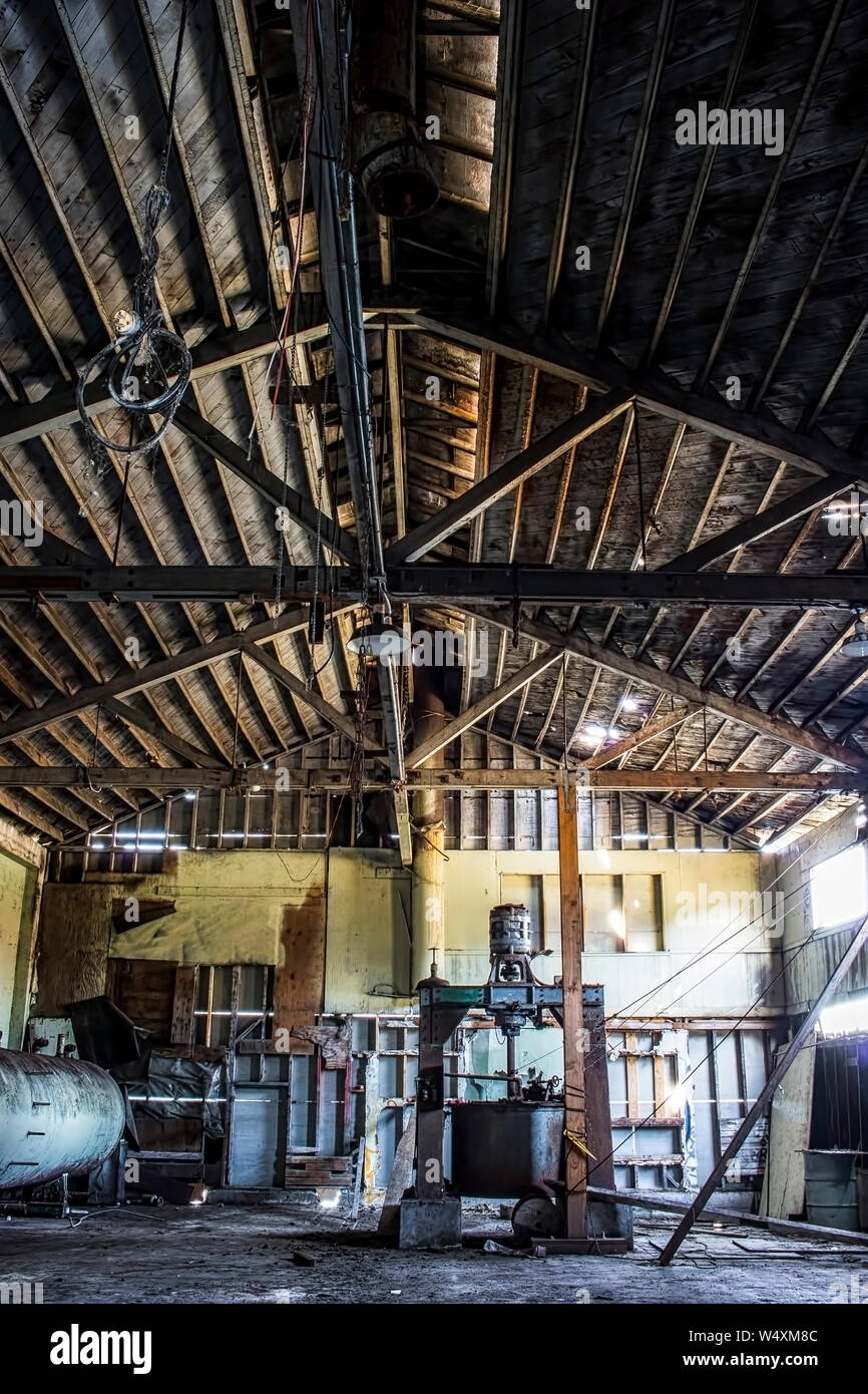 Vertical image interior of old abandoned cannery warehouse building wiht long lines of old wood running along ceiling. Stock Photo