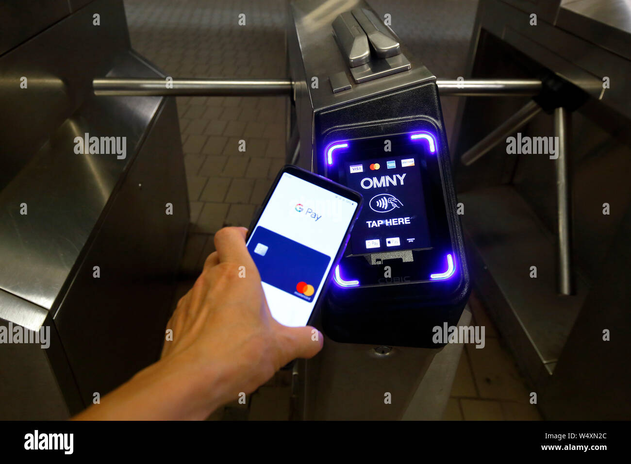 A smartphone with Google Pay taps a NYC Subway turnstile retrofitted with a contactless payment reader accepting NFC and EMV payments Stock Photo
