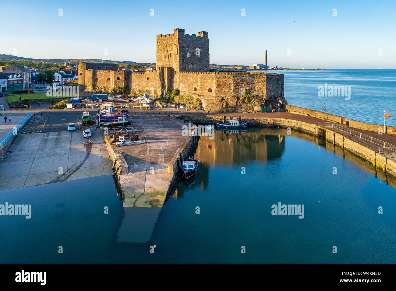 Medieval Norman Castle and harbor with boat ramp and wave breaker in Carrickfergus near Belfast, Northern Ireland, UK. Aerial view  in sunset light. O Stock Photo