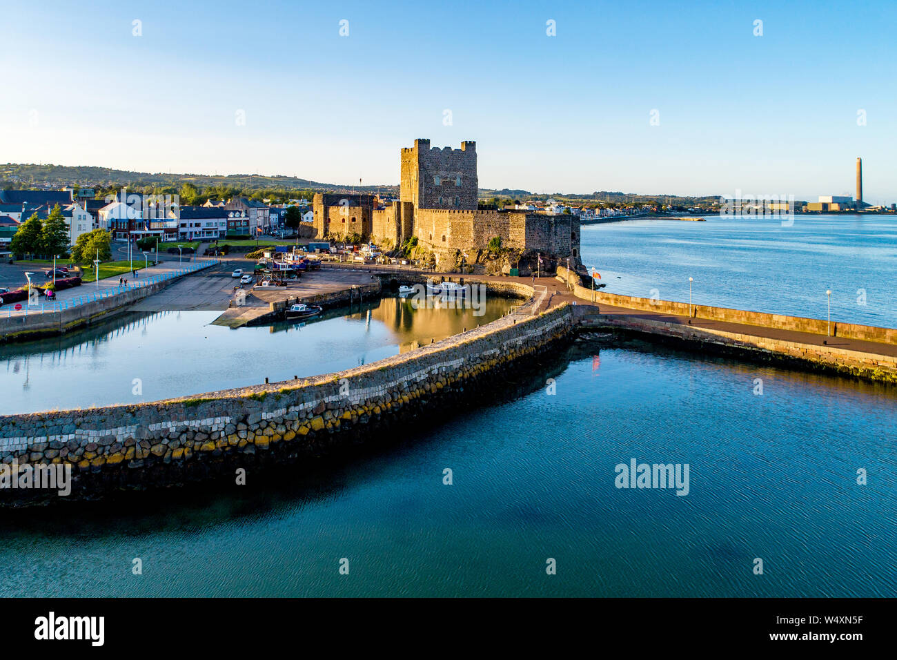 Medieval Norman Castle and harbor with boat ramp and wave breaker in Carrickfergus near Belfast, Northern Ireland, UK. Aerial view  in sunset light. Stock Photo