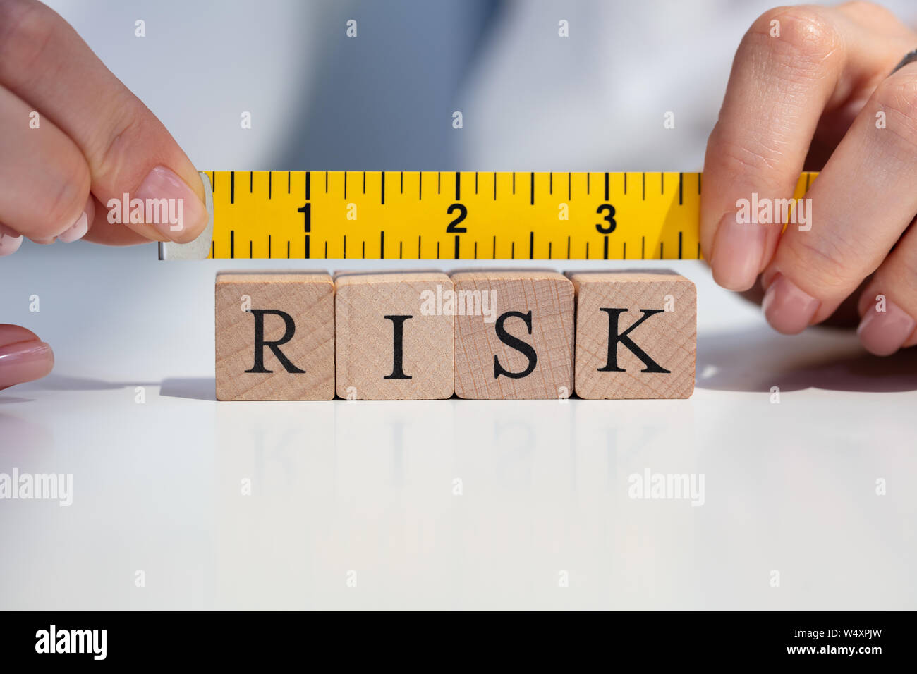 Close-up Of A Businesswoman's Hand Measuring Risk Blocks With Yellow Measuring Tape Stock Photo