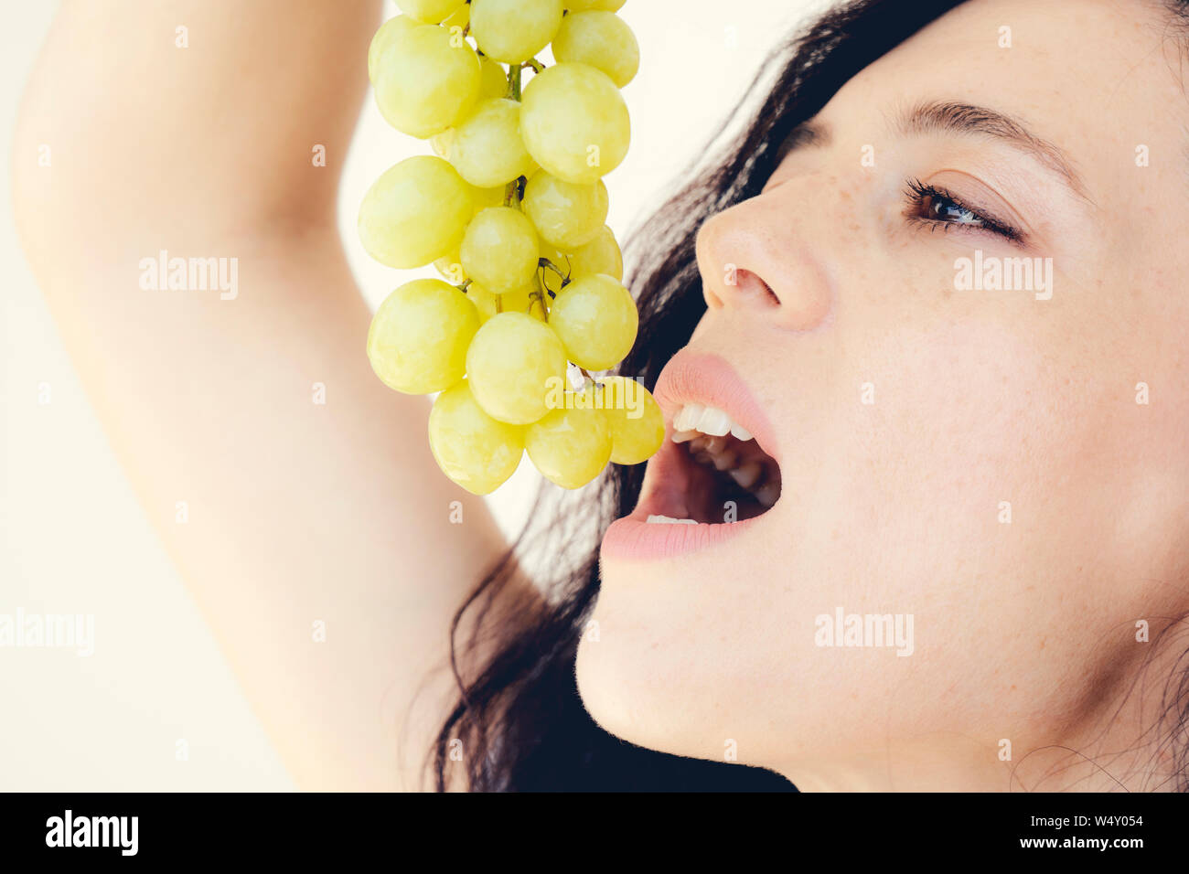 Attractive beautiful woman lifted her head up holding bunch grapes over mouth open Stock Photo