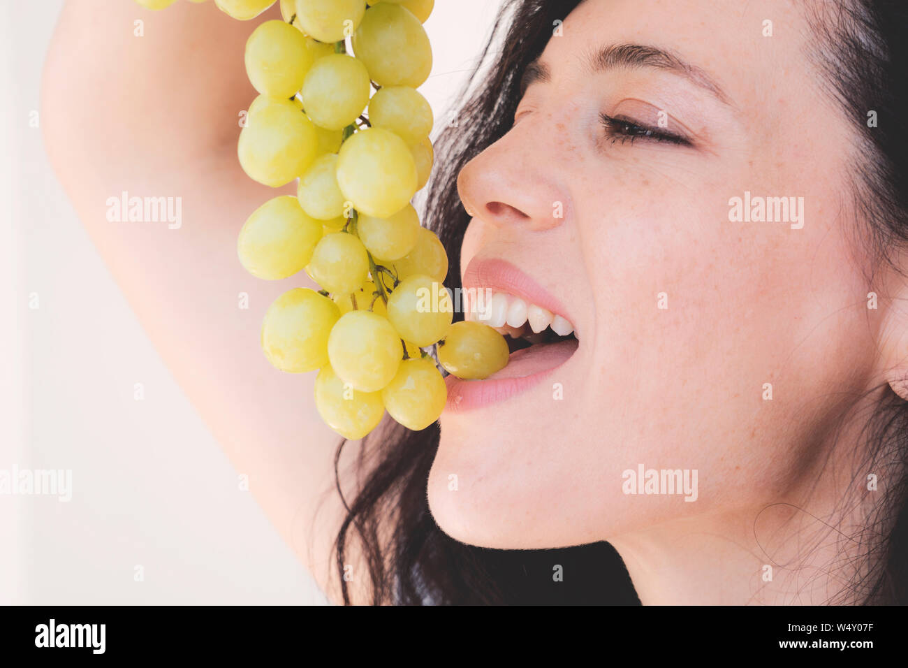 Attractive beautiful woman lifted her head up holding bunch grapes over mouth open Stock Photo